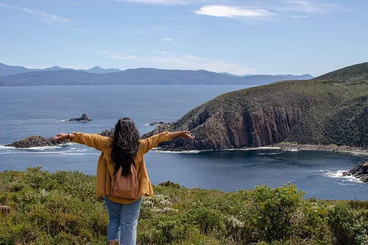 Una mujer con los brazos extendidos mirando la costa rocosa y el océano.